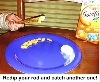 Hand using a pretzel rod with cream cheese on end to pick up goldfish crackers